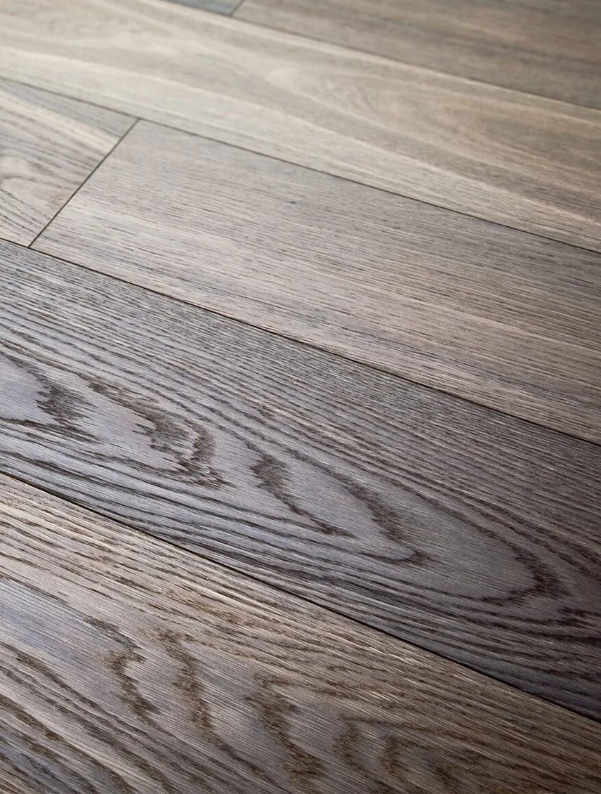 Detailní pohled na kartáčovanou dubovou podlahu v kouřově šedém odstínu z kolekce Smoke, který zvýrazňuje hlubokou texturu dřeva a jeho přirozené barevné přechody.