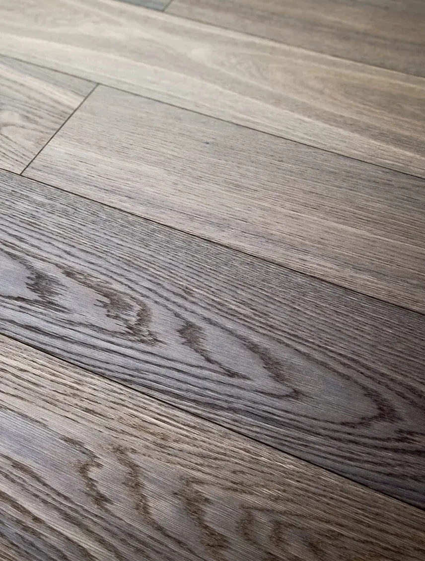 Detailní pohled na strukturu dřevěné podlahy Oakcent s výraznou kresbou letokruhů a jemným šedohnědým odstínem, který zdůrazňuje přirozený charakter masivního dřeva v rámci nabízeného servisu od výběru až po pokládku.