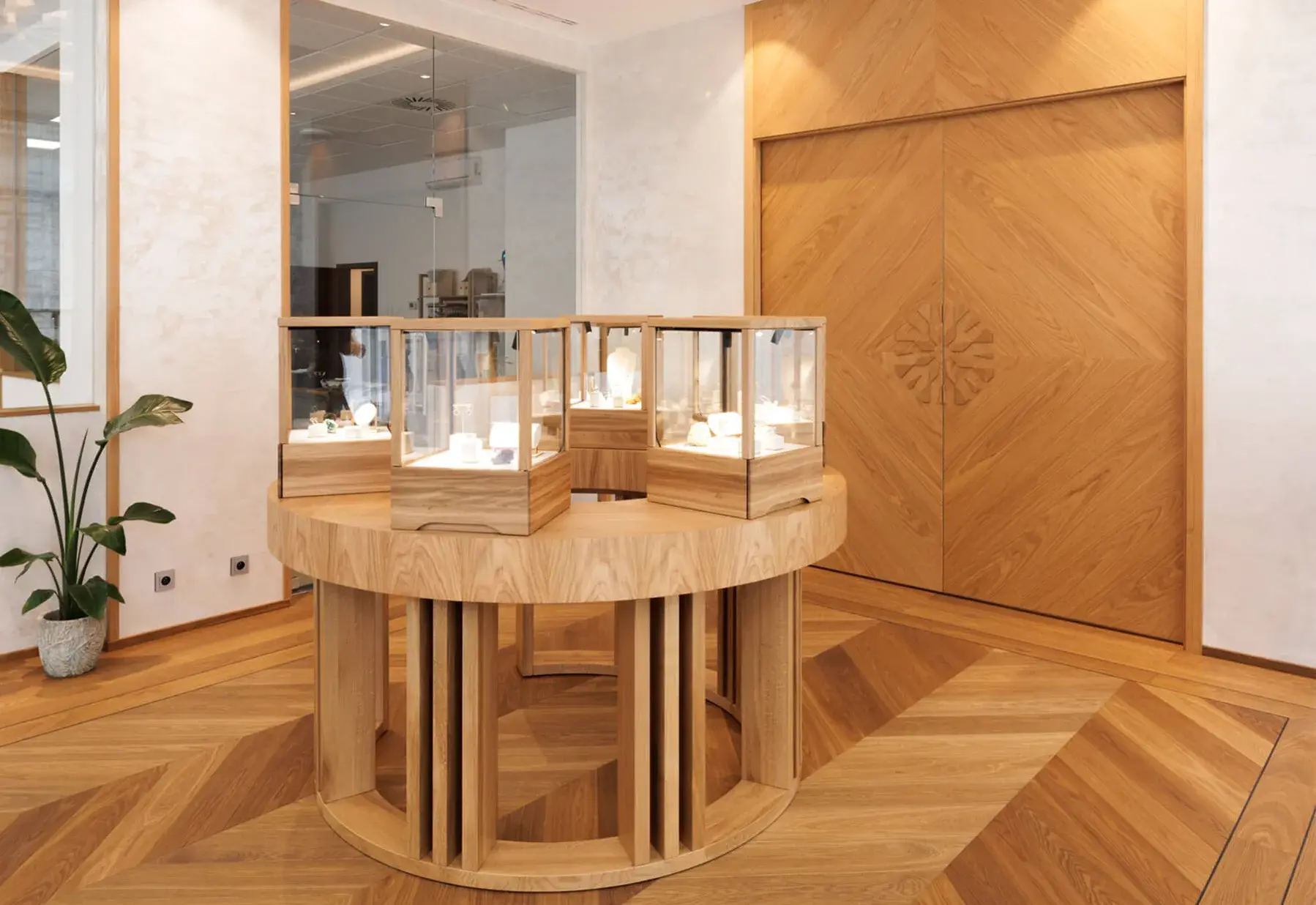 Interiér luxusního butiku nebo showroomu s dubovou podlahou v dekoru Honey položenou do vzoru maďarského stromečku (chevron), kterému dominuje kruhový dřevěný prodejní pult a zdobené dřevěné obložení stěn.