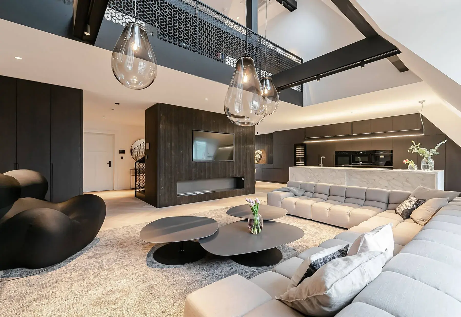 Moderní prostorný mezonetový byt s otevřeným obytným prostorem, kterému dominuje velká světlá sedací souprava, designová závěsná svítidla a kontrastní kombinace světlé podlahy s tmavým dřevěným obložením st