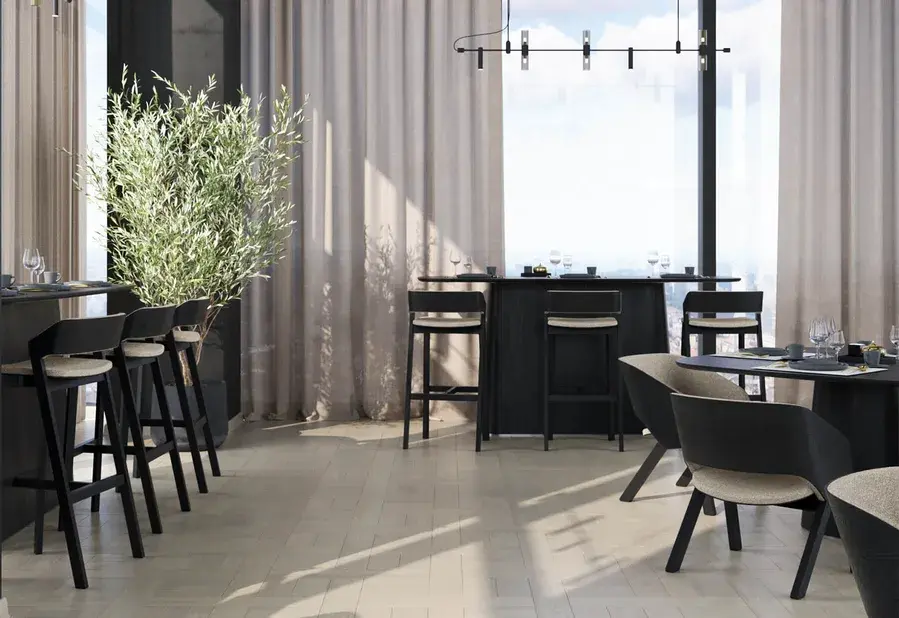 Moderní hotelový nebo barový interiér s velkými prosklenými stěnami, kde na světlou dřevěnou podlahu s geometrickým vzorem Knit dopadá denní světlo, doplněný černým minimalistickým nábytkem a olivovníkem v květináči.