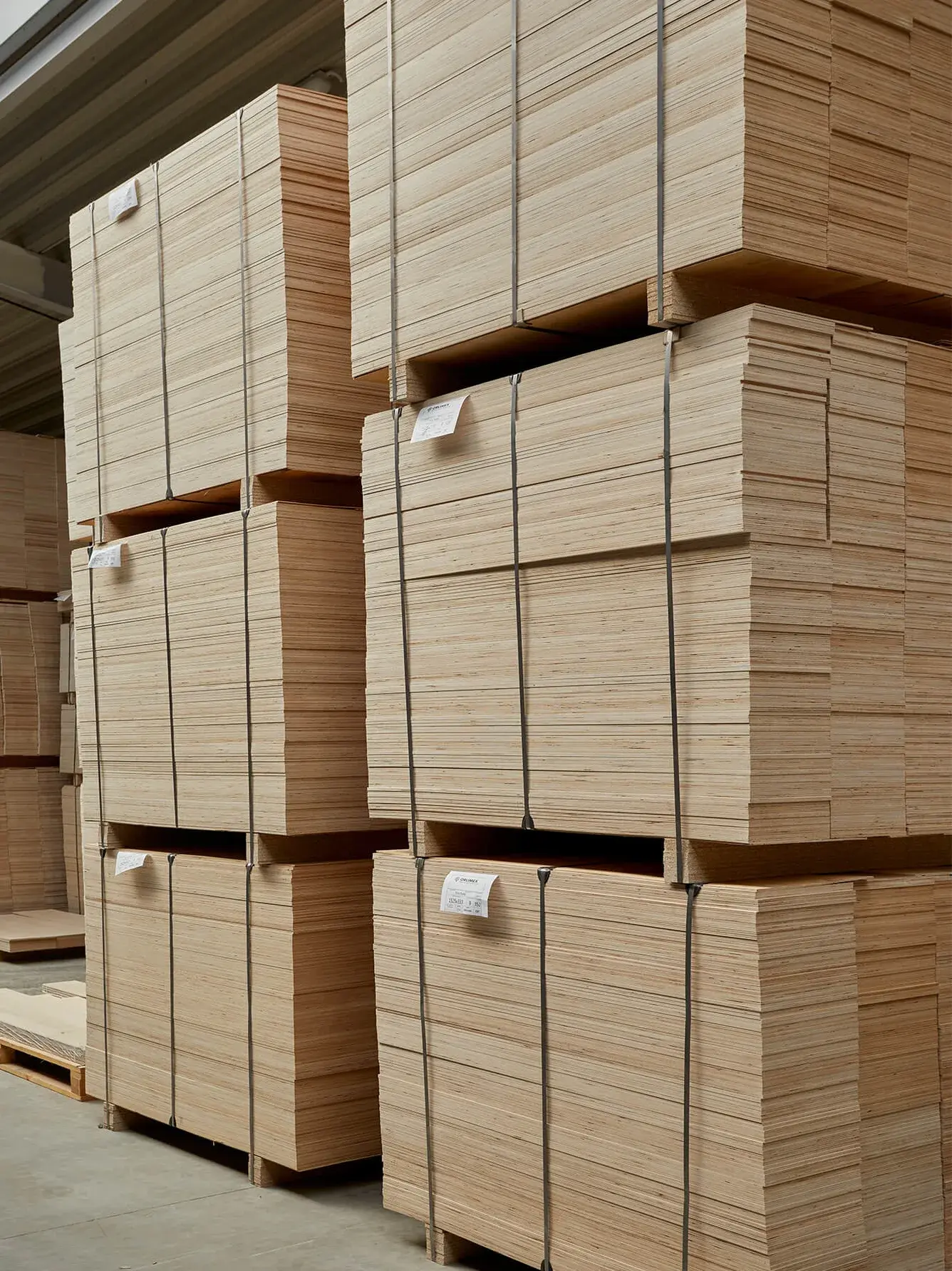 Skladové prostory s vysokými hranicemi pečlivě naskládaných dřevěných desek a polotovarů pro výrobu, připravených k dalšímu zpracování.